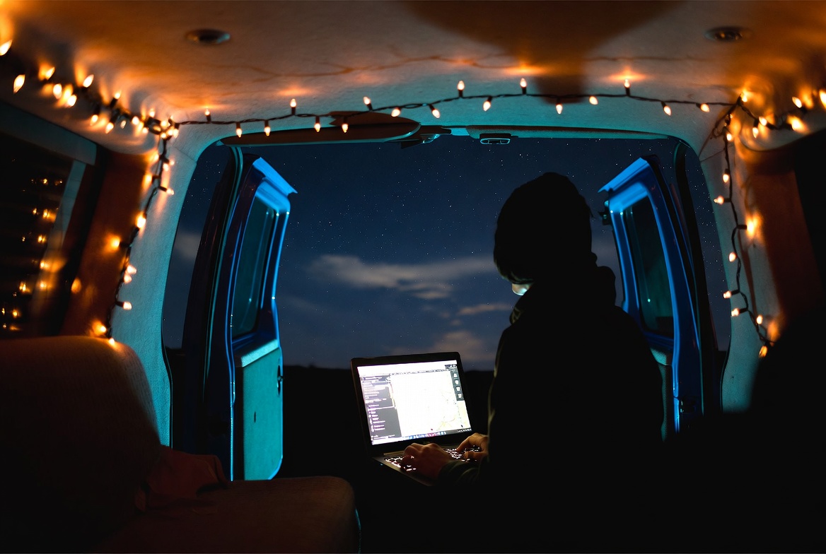 Persona trabajando con portátil en el interior de una furgoneta de noche, luces navideñas y cielo estrellado al fondo